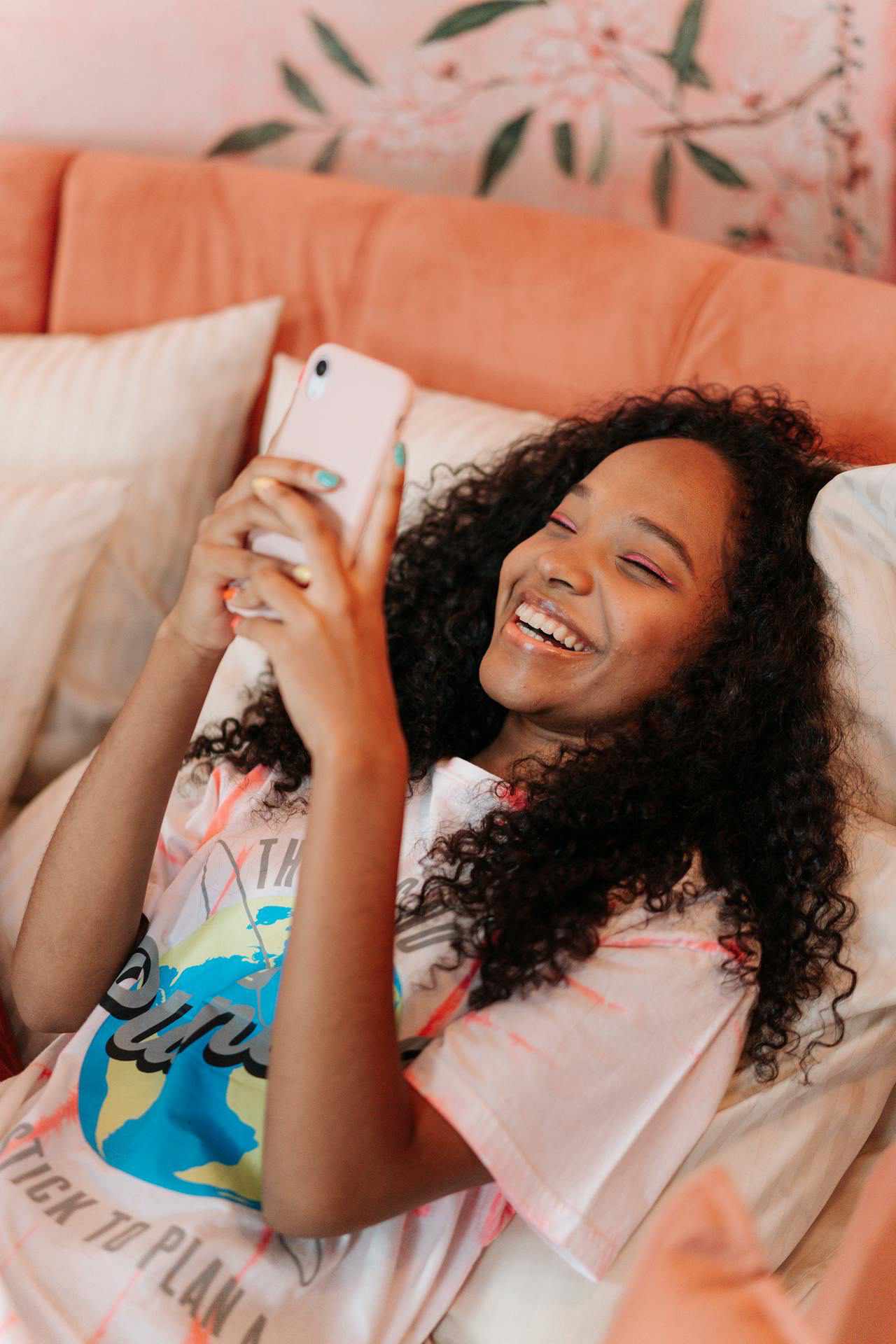 Preteen girl with long black curly hair smiling and laughing at her mobile phone while laying on the couch
