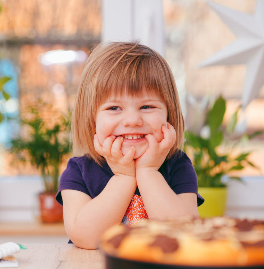 little girl sitting at kitchen counter smiling with her hands to her face