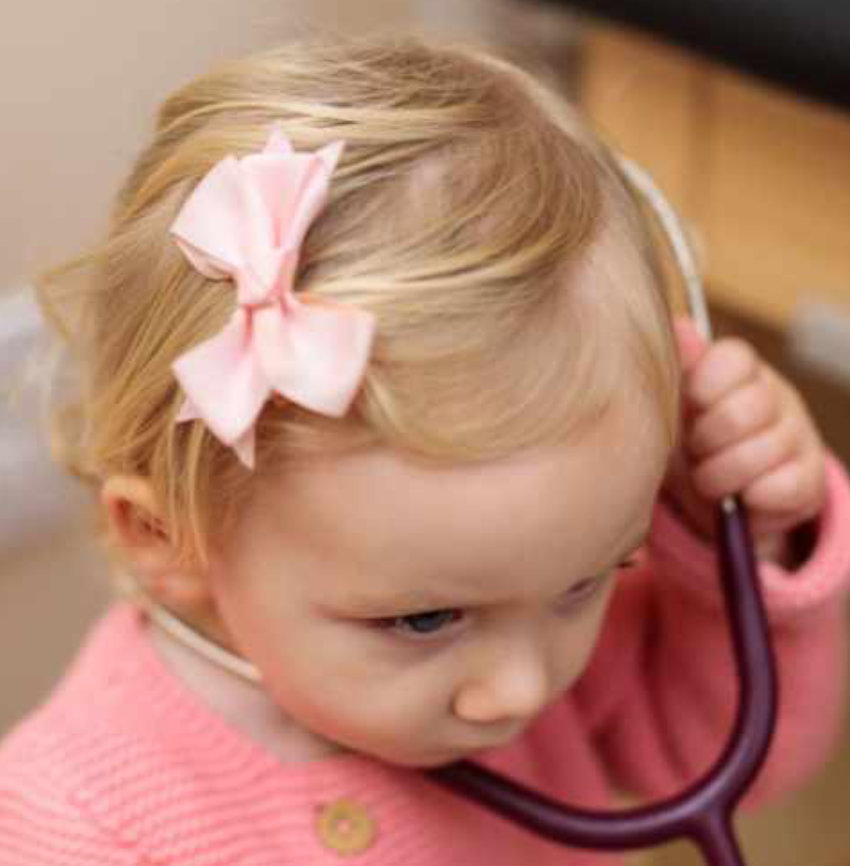 little girl with blonde hair and a big pink bow using a stethoscope